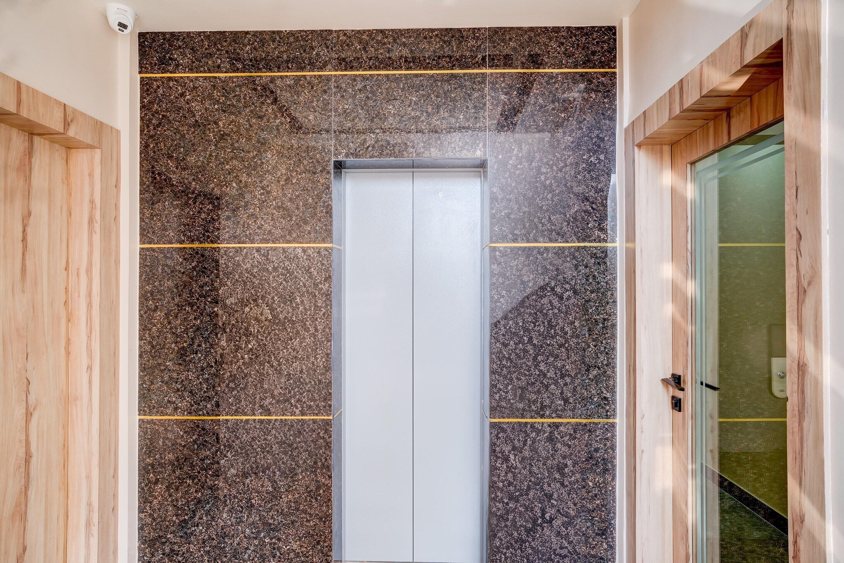 A modern elevator with a metallic interior, flanked by walls with a speckled pattern and wooden paneling.