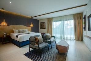 A modern hotel room with a large bed, two bedside tables, a sofa, a coffee table, and a large window with curtains.
