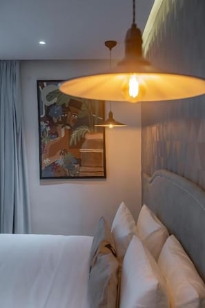 A hotel room with a bed, a hanging light fixture, and a painting on the wall.