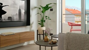 A modern living room with a large framed picture, a wooden cabinet, a round table with a vase, and a view of a balcony with red chairs. - Deluxe apartment with balcony (Split)