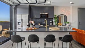Cozinha moderna com ilha central, armários escuros e um letreiro neon.