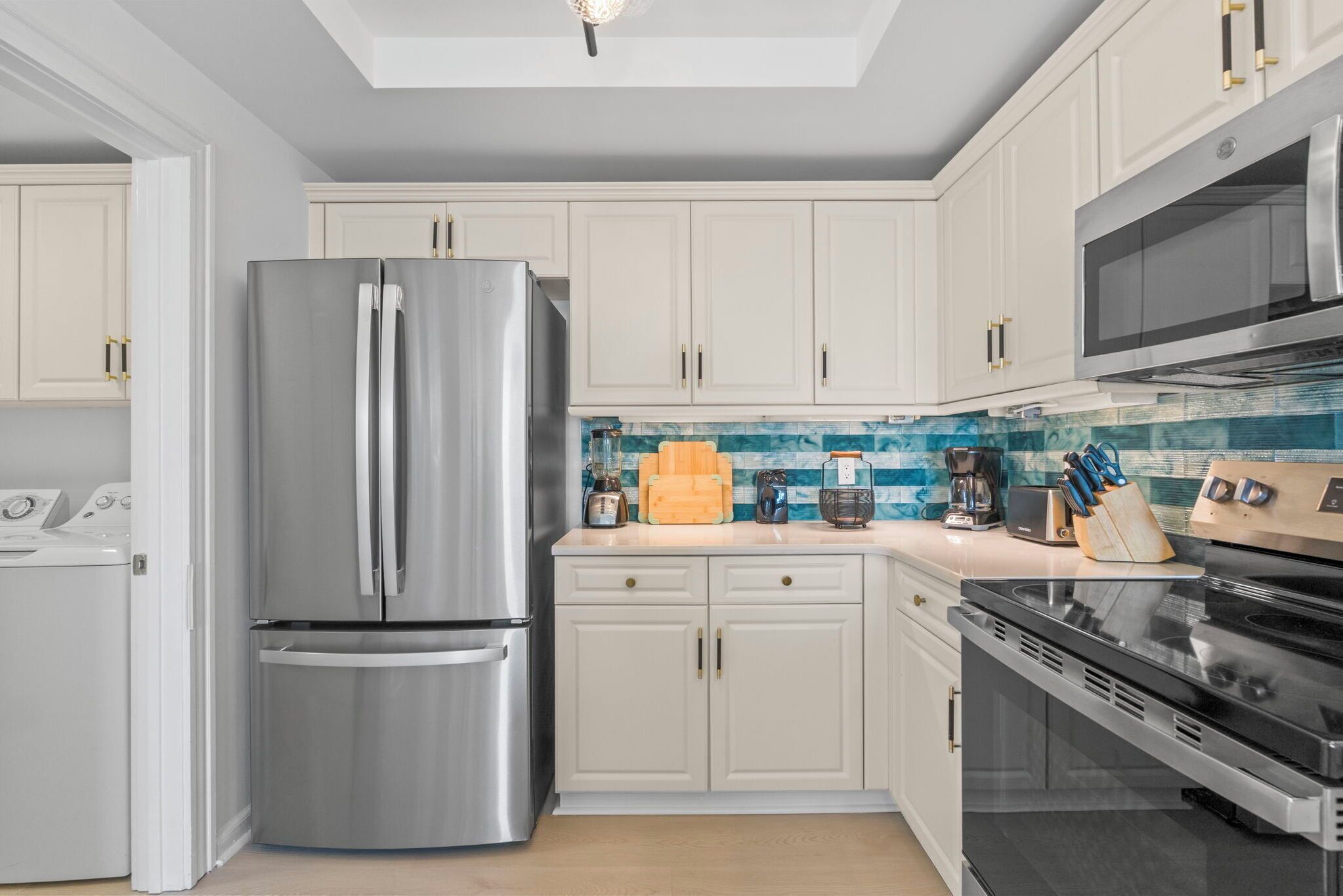 A modern kitchen with stainless steel appliances, white cabinetry, and a blue backsplash.
