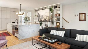 A modern living room with a black sofa, a coffee table, and a kitchen area with white cabinetry. - Luxury Retreat - Double Rooftop Deck Game Room (Nashville)