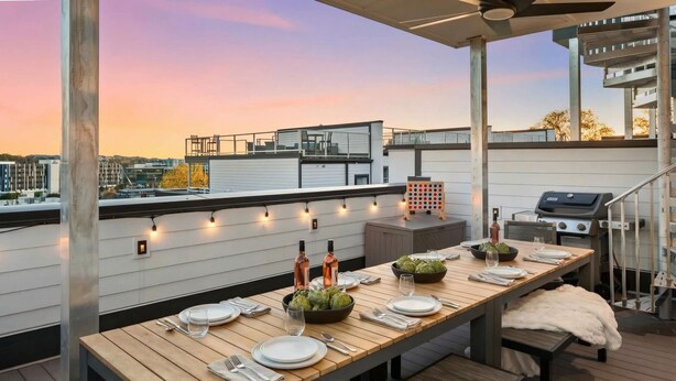 An outdoor dining area with a long wooden table set for two, a grill, and string lights. - Luxury Retreat - Double Rooftop Deck Game Room (Nashville)