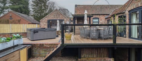 Un patio trasero con jacuzzi, mobiliario exterior y una terraza de madera.