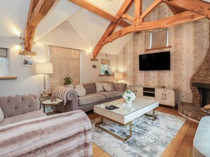 A cozy living room with a sofa, a coffee table, a fireplace, and exposed wooden beams. - Mill Race Cottage (Driffield)
