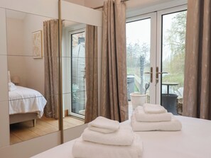 A modern bedroom with a bed, a large mirror, and a view of an outdoor area with a table and chairs. - Mill Race Cottage (Driffield)