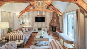 Een gezellige woonkamer met een open haard, houten balken, een zithoek en een televisie.