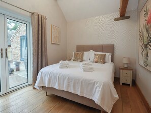 A bedroom with a bed, a nightstand, a lamp, a door, and a window. - Mill Race Cottage (Driffield)