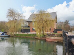A house by a canal with a boat docked nearby. - Swing Bridge Cottage (Driffield)