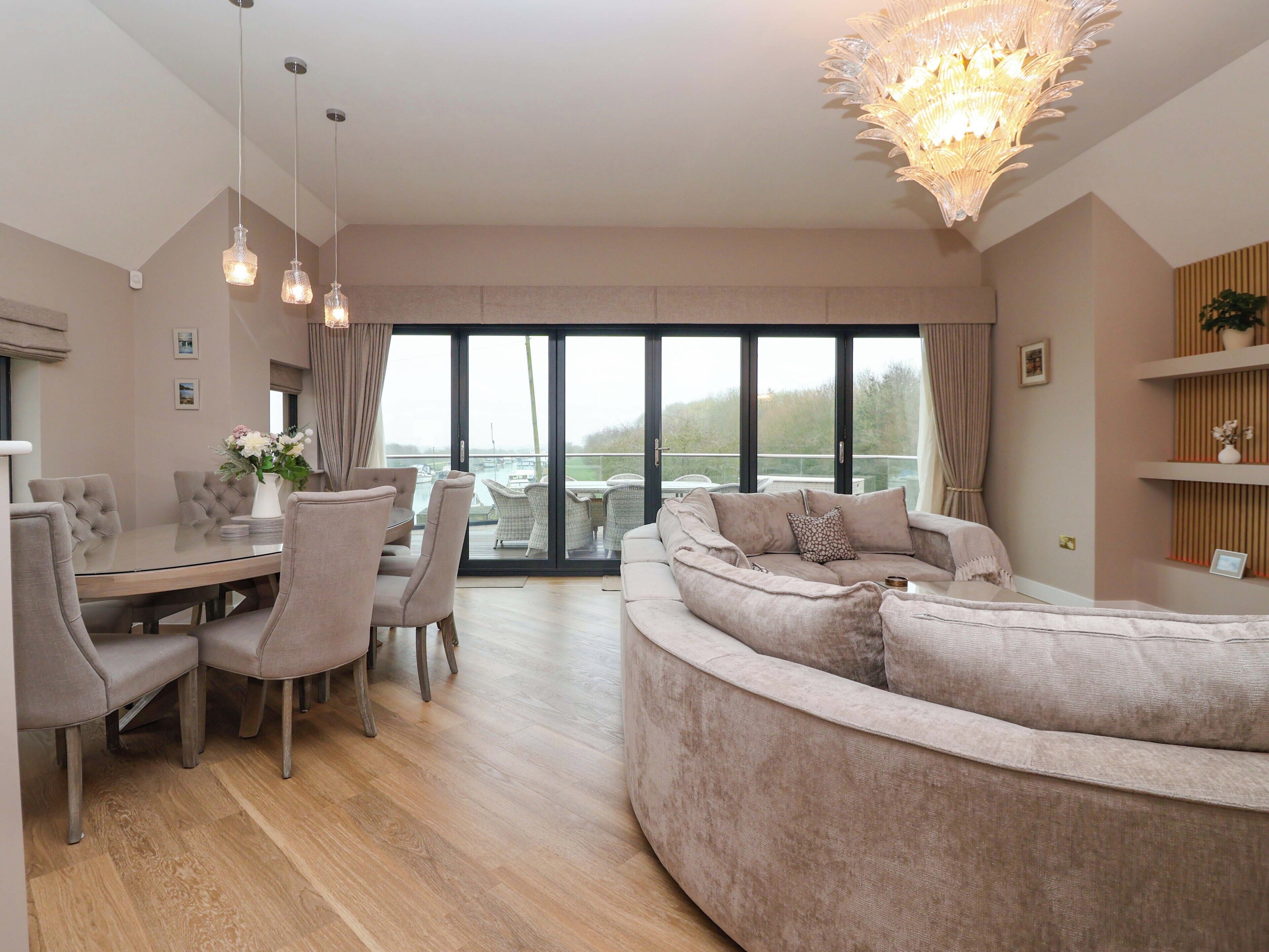 A modern living room with a glass dining area, a large sofa, and a chandelier.