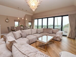 A spacious living room with a large sectional sofa, a glass coffee table, and a dining area with chairs and a table. - Swing Bridge Cottage (Driffield)