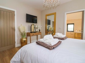 A hotel room with a bed, a vanity with a mirror, a TV mounted on the wall, and a door leading to another room. - Swing Bridge Cottage (Driffield)