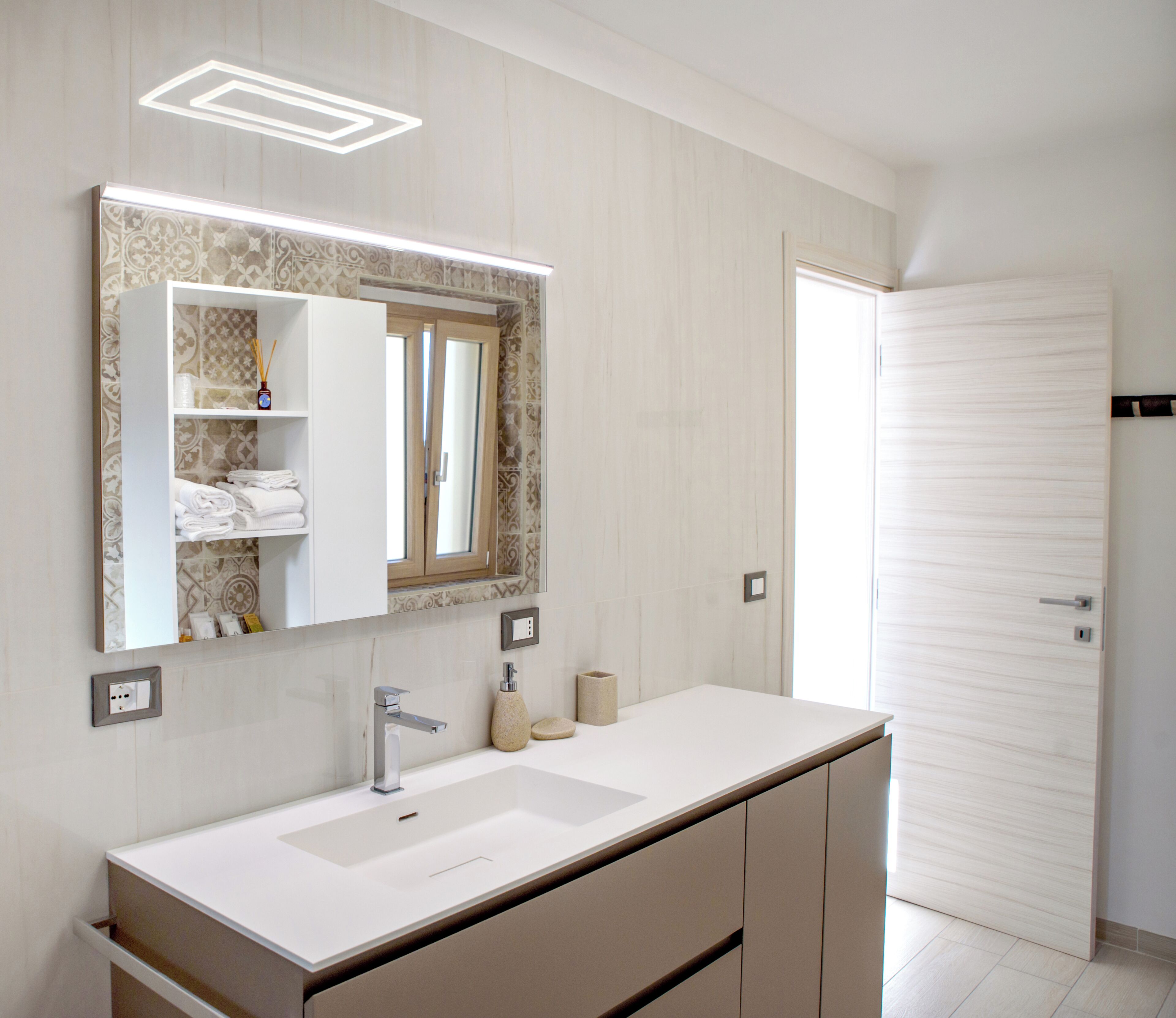 A modern bathroom with a large mirror, two sinks, a towel rack, and a toilet.