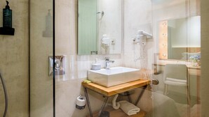 Un baño moderno con cabina de ducha de vidrio, tocador de madera con lavamanos blanco y espejo con luces.