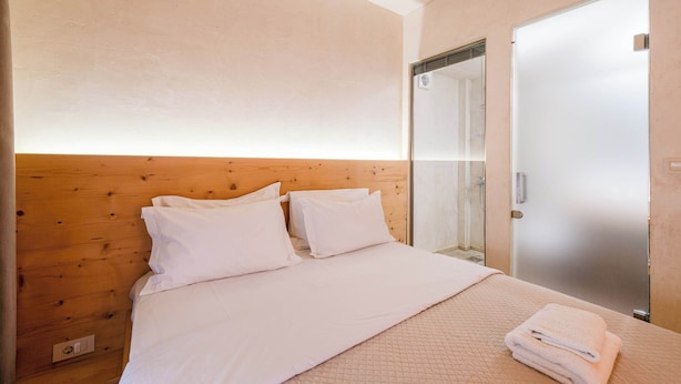 Un dormitorio con cabecera de madera, cama con ropa blanca, una toalla doblada sobre la cama y una puerta de vidrio esmerilado.
