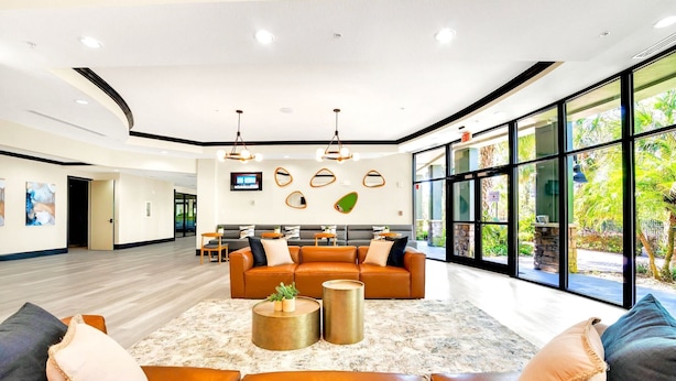 A spacious lobby with a large seating area, a flat-screen TV mounted on the wall, and large windows offering a view of the outdoors. - Upstay Modern 2BR Condo Near Disney (Winter Garden)