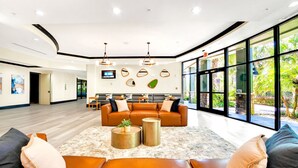 A spacious lobby with a large sofa, a coffee table, and a TV mounted on the wall. - Upstay Modern 2BR Condo Near Disney (Winter Garden)