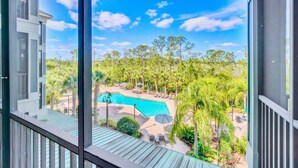 A view of a swimming pool surrounded by palm trees and lounge chairs, with a clear blue sky above. - Upstay Modern 2BR Condo Near Disney (Winter Garden)