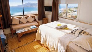 Un dormitorio con cama, un banco, vista al océano y una ventana.