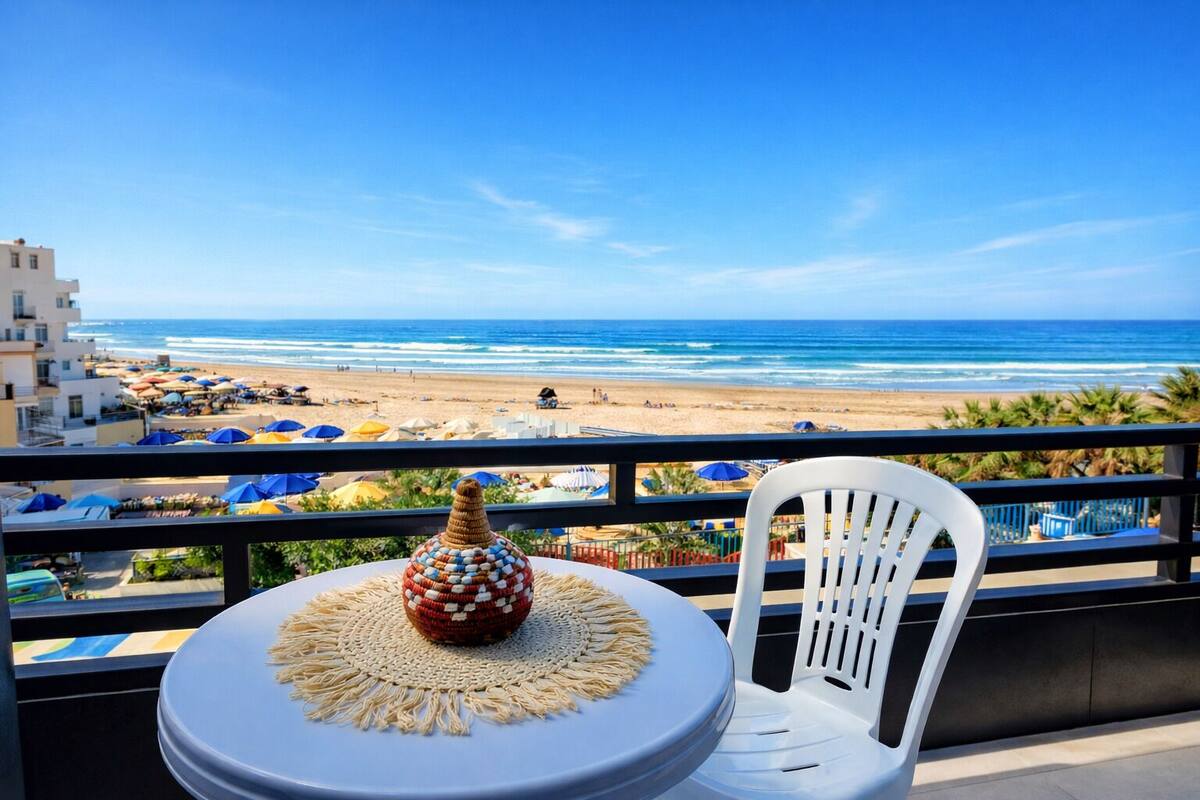 A balcony with a view of the beach, a woven basket, and a white chair.