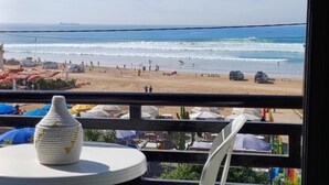 Vista a la playa desde un balcón, con un florero sobre una mesa, sombrillas y sillas de playa.