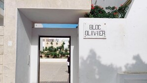A building entrance with a sign reading 'BLOC OLIVIER,' a paved pathway, and a view of a courtyard with palm trees. - Peaceful 1-bedroom apartment with AC in charming La Marsa (La Marsa)