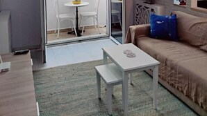 A living room with a sofa, a coffee table, a sliding glass door leading to a balcony with chairs and a table, and a brick wall with shelves. - Peaceful 1-bedroom apartment with AC in charming La Marsa (La Marsa)