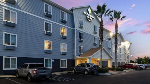 A hotel with multiple floors, a sign for 'Woodspring Suites,' and several vehicles parked in the lot. - Woodspring Suites Jacksonville East 295 Cruise Port (Jacksonville)
