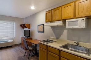 Una cocina compacta con armarios de madera, un microondas, un fregadero, una estufa, una silla y una mesa pequeña.