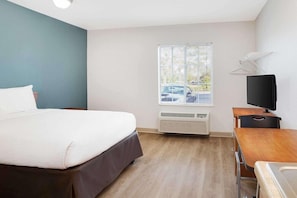 Quarto de hotel com uma cama, uma escrivaninha com cadeira, televisão e janela com persianas.