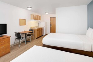 A compact hotel room with a single bed, a desk with a chair, a small kitchenette, and a television. - Woodspring Suites Jacksonville East 295 Cruise Port (Jacksonville)
