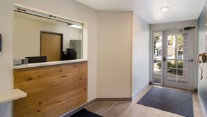 A hallway with a wooden panel wall, a mirror, a door with glass panels, and a doormat. - Woodspring Suites Jacksonville East 295 Cruise Port (Jacksonville)