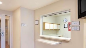 A hotel reception area with a check-in/check-out sign, a clock, and a framed certificate on the wall. - Woodspring Suites Jacksonville East 295 Cruise Port (Jacksonville)