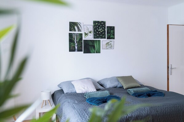 A bedroom with a bed, pillows, a bedside table, a wall with framed pictures, and a door.