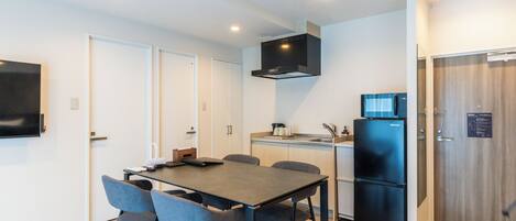 A modern kitchen with a dining area, a black refrigerator, and a flat-screen TV mounted on the wall.