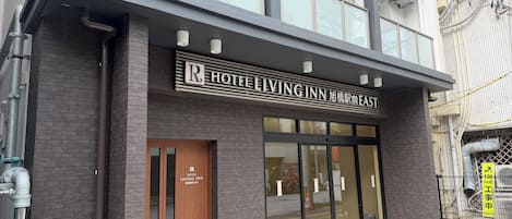 Entrada de un hotel con un cartel que dice 'Hotel Living Inn' y una 'R' visible que indica habitaciones disponibles.