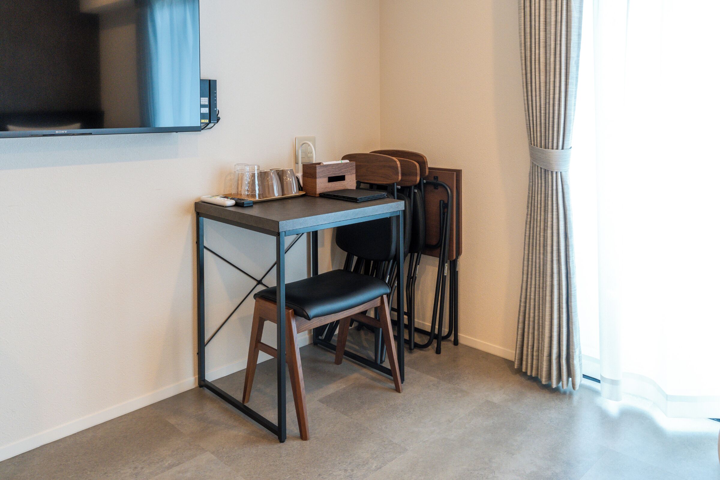 A modern room with a desk, chairs, a television, and a window with curtains.