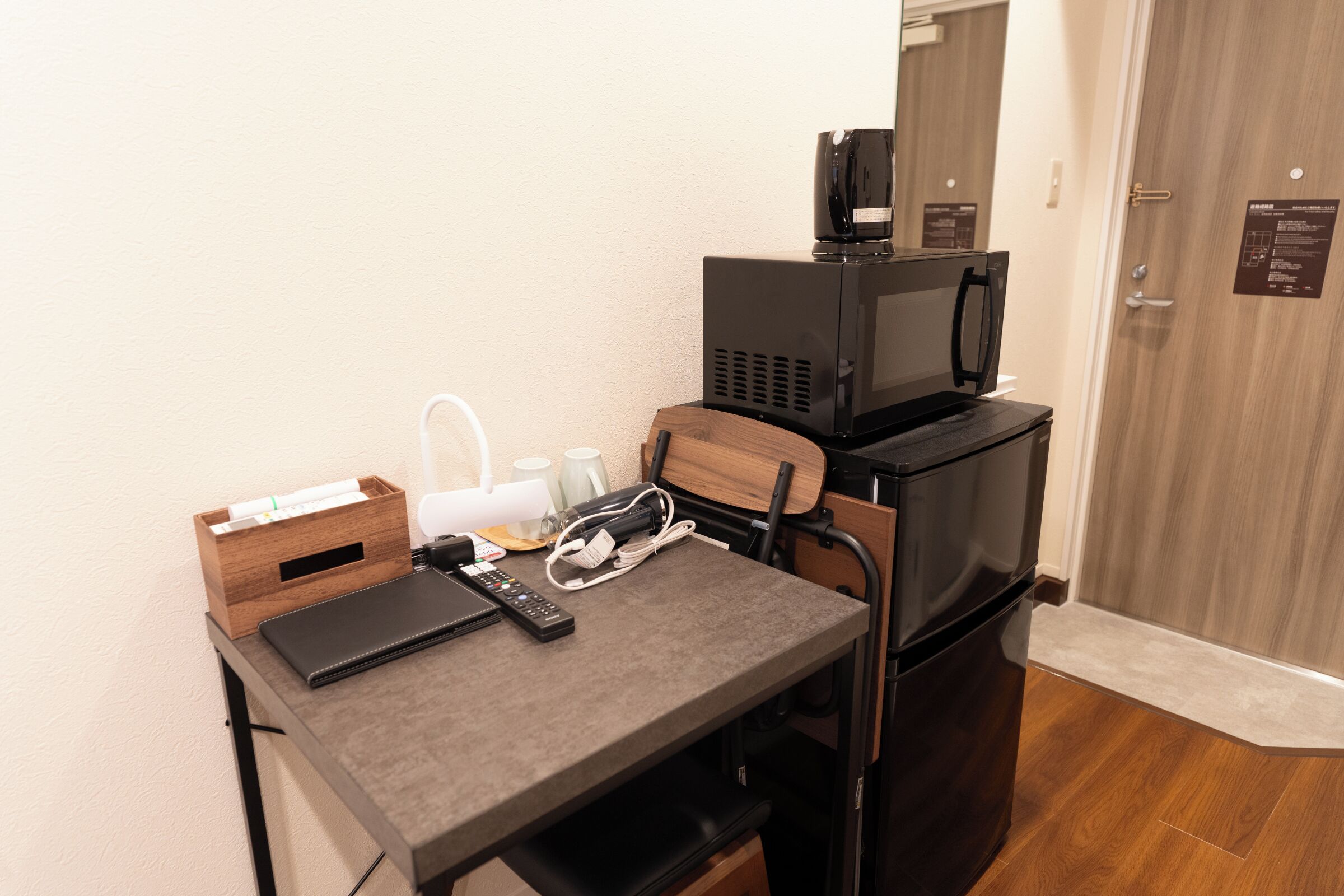 A compact kitchenette with a microwave, a coffee maker, and a small table with a remote control and a notebook.
