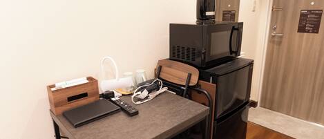A compact kitchenette with a microwave, a coffee maker, and a small table with a remote control and a notebook.