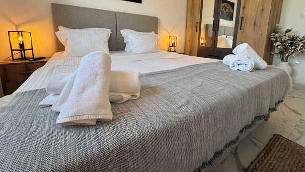 Un lit bien fait, avec du linge de lit et des serviettes blanches, un grand miroir et une œuvre d’art accrochée au mur.