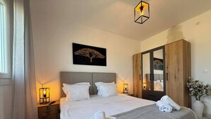 Een opgemaakt bed met kussens, een bedlamp, een spiegel en een lijst met een kunstwerk aan de muur.