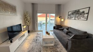 Een moderne woonkamer met een flatscreen televisie, een grijze bank, een salontafel en een groot raam met uitzicht.