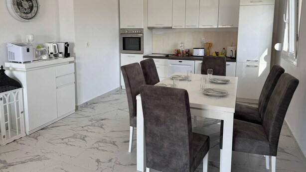 Een moderne keuken met witte kastjes, een eettafel met stoelen en een klok aan de muur.