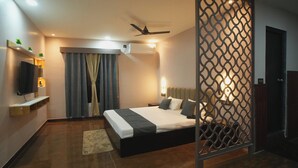 A modern hotel room with a bed, ceiling fan, air conditioning unit, TV, and a decorative partition. - Kasa Courtyard (Begusarai)