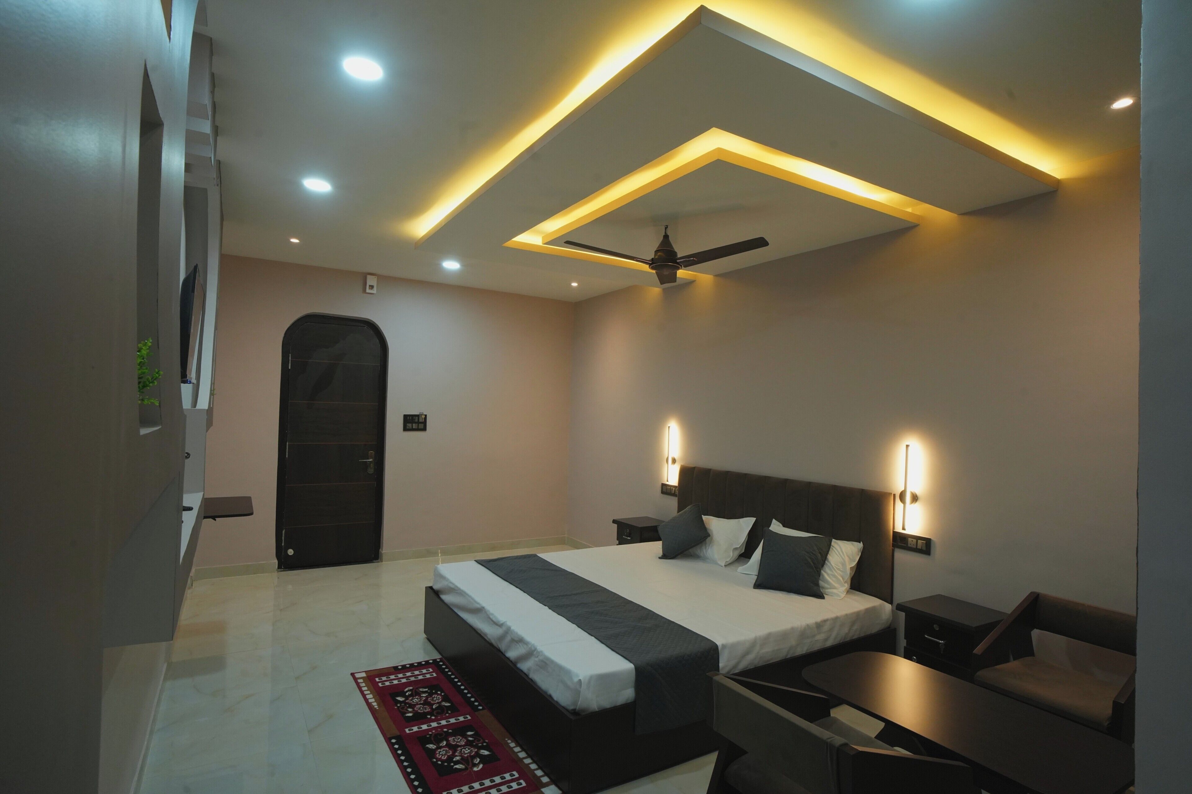 Une chambre moderne avec un lit, des tables de chevet, un ventilateur de plafond, un éclairage encastré et un tapis rouge à motifs.