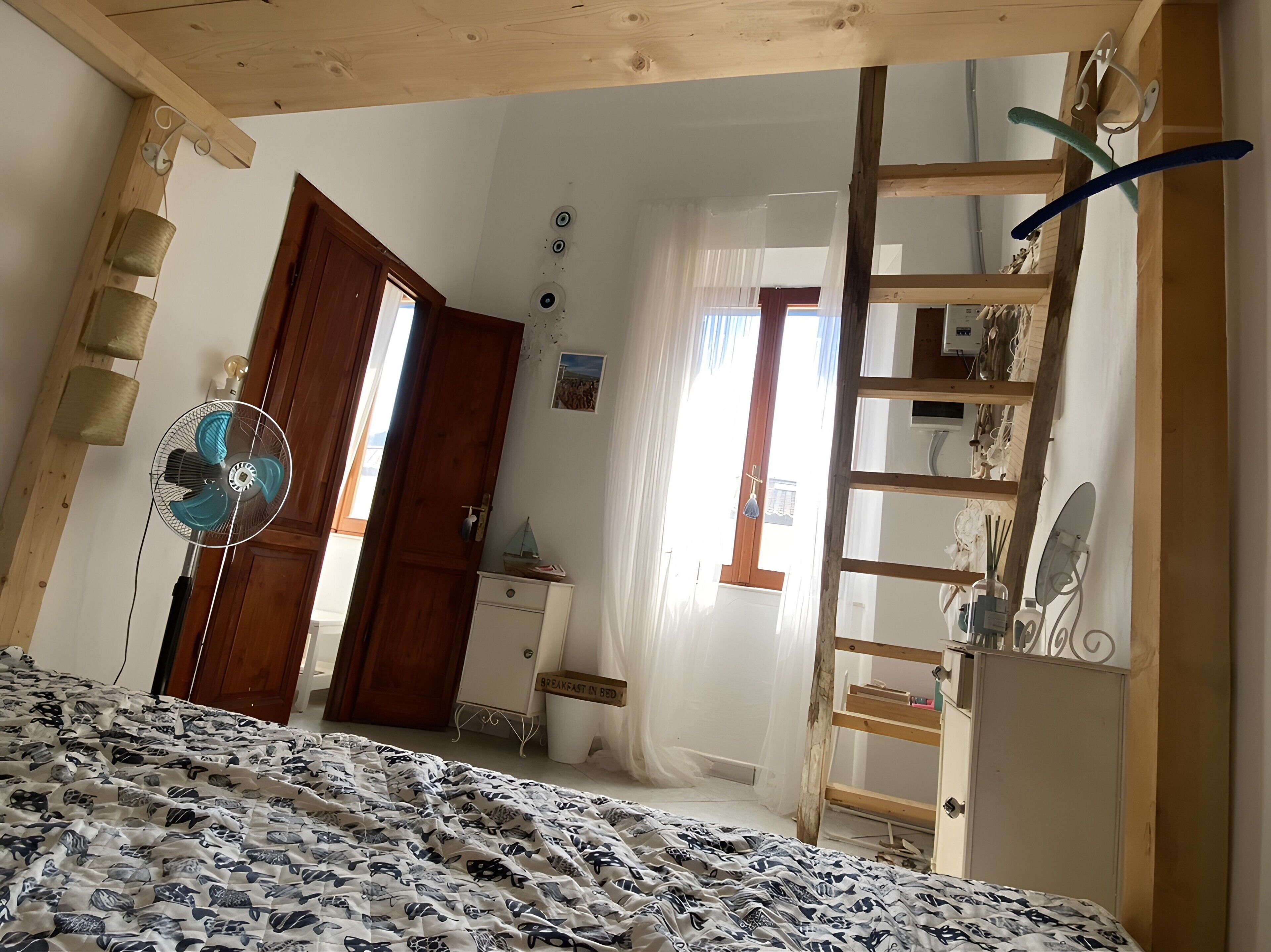 A bedroom with a bed, a wooden ladder, a dresser, a fan, and a door.