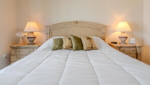 Een net opgemaakt bed met hoofdbord, twee nachtkastjes met lampen, en een bordje dat uitzicht op zee aangeeft.