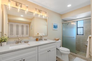 A modern bathroom with a large mirror, a sink, a toilet, and a shower area. - Island Winds Penthouse 1 (Fort Myers Beach)