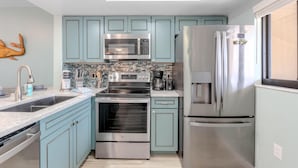 A modern kitchen with teal cabinetry, stainless steel appliances, and a tiled backsplash. - Bac Bay #223 (Fort Myers Beach)